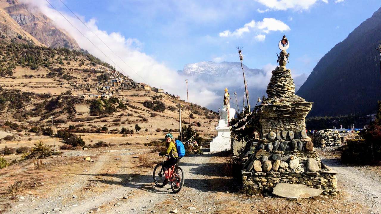 A biker carrying a blue bag is taking some time to take a picture with the back-drop of Pisang village in Manang.