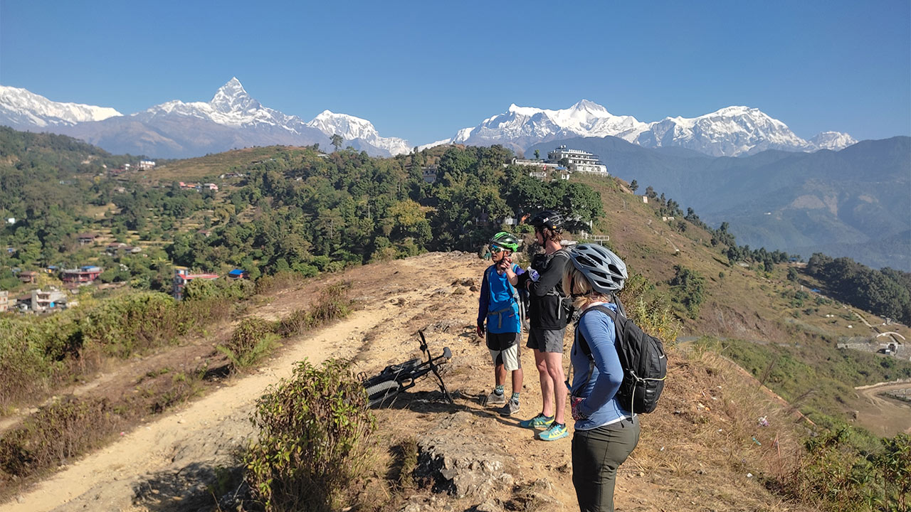 Three mountain bikers are observing the incredible views of Pokhara valley and the Annapurna mountain range from Gyarjati.