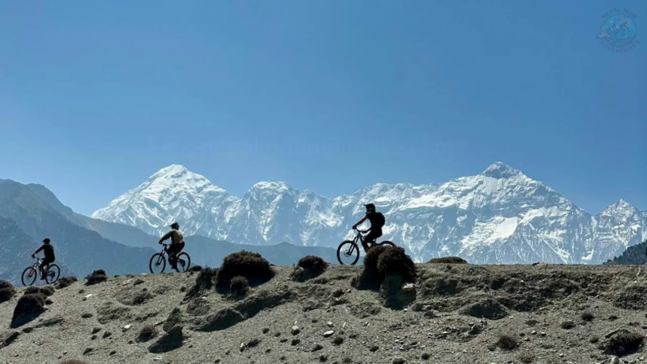 Enduro bikers riding their bikes with the view of Tilicho and Nilgiri Peaks during Nepal enduro MTB tour in Mustang.